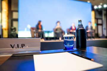 VIP seating, with plain white paper, a pencil, a glass of water, and a bottle of water on a desk...