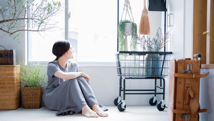 明るい植物のある窓辺の部屋で座って空を見上げて休憩する日本人女性