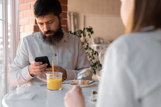 Cheerful spouses using smartphone while eating breakfast in kitchen, happy couple enjoying tasty morning meal, shopping online or checking social networks on cellphone