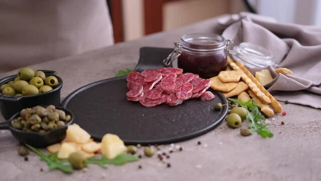 woman puts slices of fuet sausage onto stone serving board at domestic kitchen