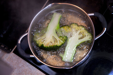 Broccoli inflorescences cut lengthwise are cooked in boiling water in a saucepan