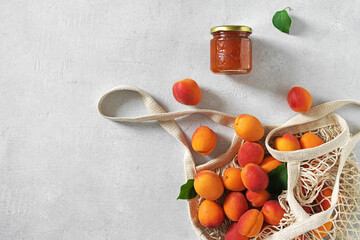 apricots in string bag and jar with apricot jam on white table. copy space. top view