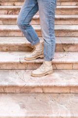 Woman's legs in blue twisted jeans and in beige boots on pink marble staircase. Front view, vertical photo