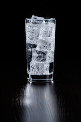 Sparkling mineral water with ice in a transparent glass on a black background.