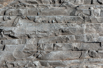 Stone gray wall with dark spots and various patterns and bulges. Textured stone background is gray with various damages.