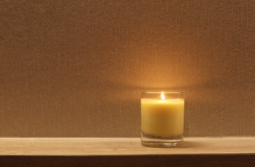 Obraz na płótnie Canvas a burning luxury aromatic scented candle glass is on wooden table and background of wooden texture wall of the luxury bed room to creat relax and romantic ambient during valentine day