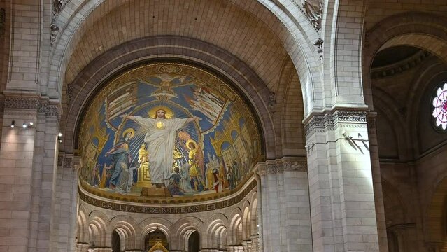 Paris, France, June 2022. Tilt footage inside the Sacre Coeur Basilica. In the apse, the large golden mosaic with Christ in the center of the scene with his arms outstretched.