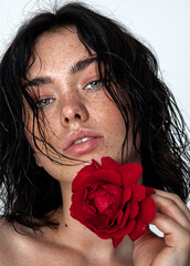 beauty young woman face with a lot of freckles and natural lips, red rose near face, close up