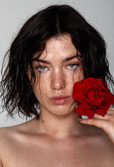 beauty young woman face with a lot of freckles and natural lips, red rose near face, close up