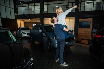 Fototapeta na wymiar Happy caucasian couple hugging while buying a new car in a car dealership.