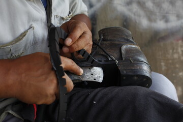 Repairing broken shoes by a shoe repairman. Cut the edges of the treads that have been replaced by rubber treads using a cutter. Isolated on a shoe repairman manually.