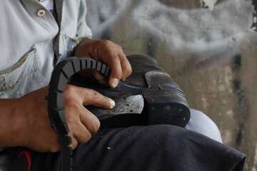Cut the edges of the treads that have been replaced by rubber treads using a cutter. Isolated on a shoe repairman manually. Isolated on Repairing broken shoes by a shoe repairman.