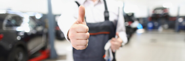 Male worker in uniform showing thumbs up posing in garage