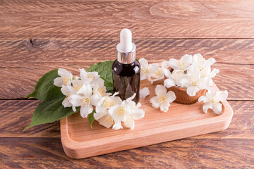 facial serum with jasmine oil extract in a cosmetic bottle stands on a wooden tray among white fragrant flowers. additional care.