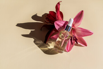 a bottle with a dropper with a serum for the face or organic oil for self-care lies on the flowers of the lily. the concept of natural cosmetics.