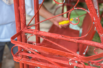 A handyman paints old glider swing made of wrought iron with red oxide primer paint. Restoring or...