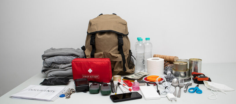 Emergency Backpack Equipment Organized On The Table. Documents, Water,food, First Aid Kit And Another Items Needed To Survive.