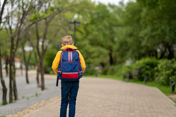 Obraz premium boy in a yellow sweatshirt with a backpack on his back going to school. back to school concept 