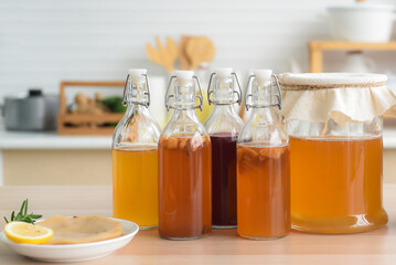Homemade fermented raw kombucha tea, variety of flavors in bottles and glass jars mix with a fruit juice and scoby on wooden table in kitchen. Healthy natural probiotic drink.