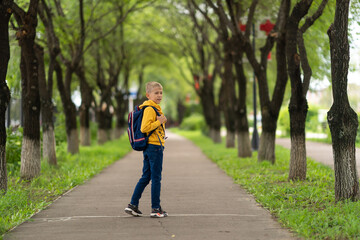 a blond boy in a yellow sweatshirt and a backpack over his shoulders going to school