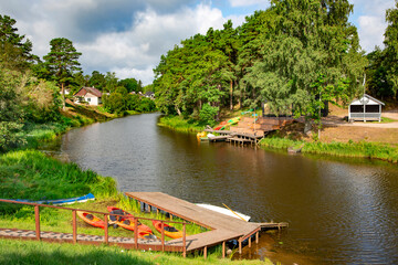 Roja river flows through a small cozy town of the same name and flows into the Baltic Sea. Roja, province of Latvia. Modern kayaks with paddles on beach near river.