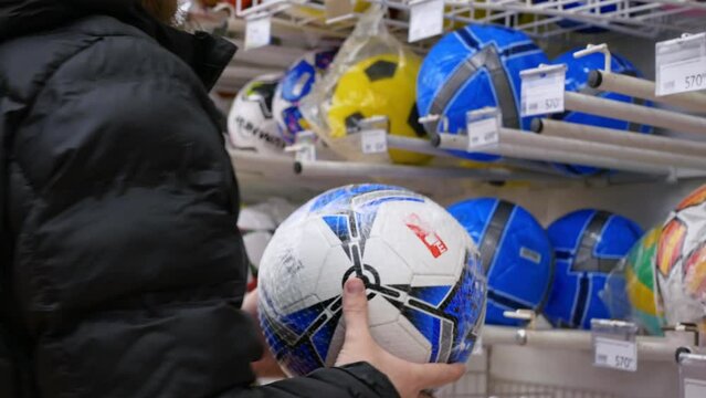 A man in a shop chooses a new soccer ball. Purchase of sports equipment for team games in a sports store. Buying a soccer ball to play your favorite hobby around the world. The most famous football