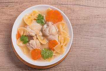 Macaroni soup with chicken thighs in clear broth with carrots.on an rustic old wood background.