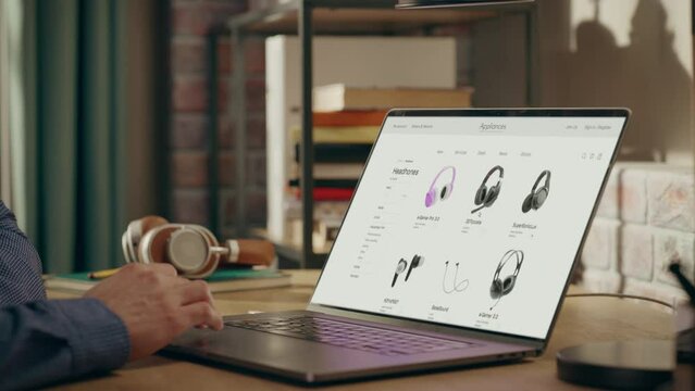 Man Using Laptop Computer, Online Shopping for Electronics, Wireless Hi-Fi Headphones. e-Commerce Concept of Purchasing, Buying, Ordering Tech Devices on Website. Over Shoulder Close-up Screen Shot