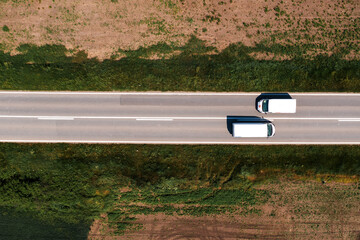 Aerial shot of two white van vehicles passing by each other on highway through countryside...