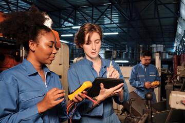 Two professional female engineer workers in safety uniforms work by inspecting machines' voltage current, checking, and maintaining at manufacturing factory, electric system service occupations.