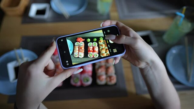 Girl take pictures of sushi in cosy japanese restaurant, using smartphone. Female hands take photos of food by modern smartphone. Close up, 4K