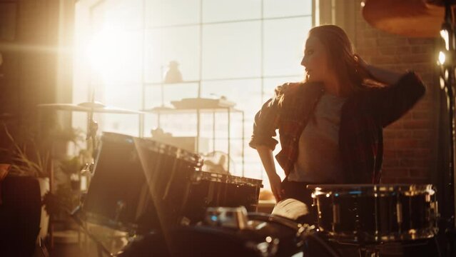 Beautiful Young Drummer Playing at a Band Rehearsal, Doing Tricks with Drumsticks. Female Checks Her Smartphone Notifications in Sunny Living Room Loft Apartment.