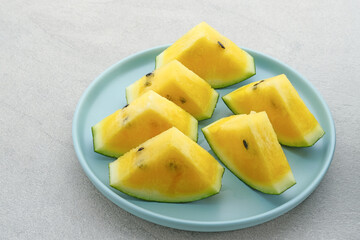 Slice yellow watermelon or semangka kuning in tosca plate on grey background. Selective focus.
