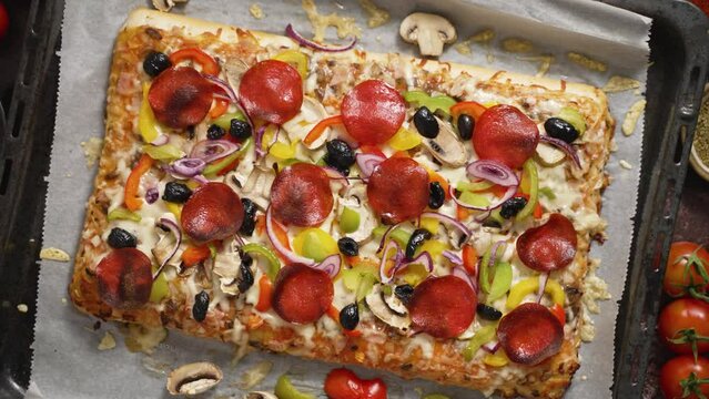 A piece of square pizza with basil pepperoni tomatoes and mushrooms on a iron tray