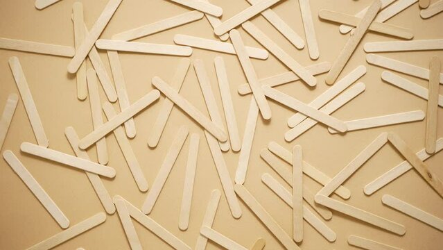 Wooden popsicle sticks, scattered on top of a beige background