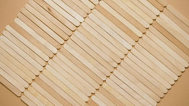 Wooden popsicle sticks, placed in a rows on top of a beige background