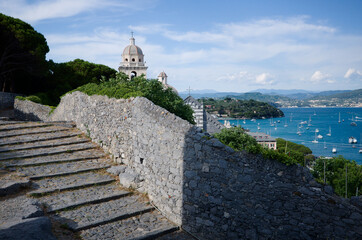 Panoramic view to bay with many yachts from stone steps and remains of medieval stone wall in Porto Venere, Italy. Dome of San Lorenzo church and roof with religious cross is visible in background