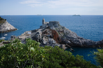 View of Chiesa San Pietro or St. Peter Church in Porto Venere, Liguria, Italy. View of medieval church on rock by sea. Cruise ships are on horizon.  Attraction of Italian Riviera near La Spezia