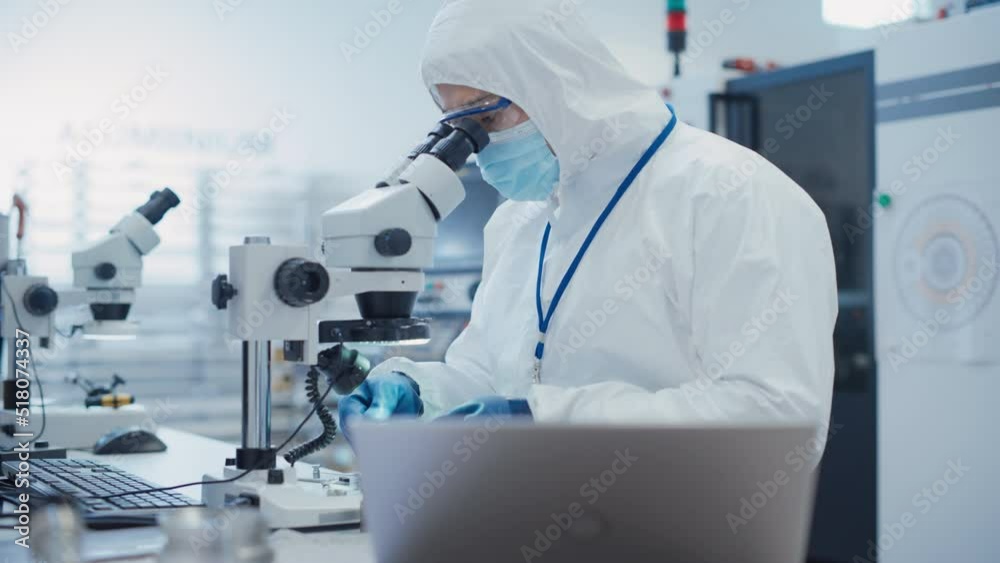 Leinwandbilder Electronic Manufacturing Factory: Engineer in Sterile Coverall Working on Laptop Computer, Examining a Circuit Board with Microchips Through a Microscope and Testing New Electrical Equipment.