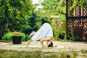 Young woman practices yoga in courtyard of a country house. Headstand - Ardha Salamba Shirshasana