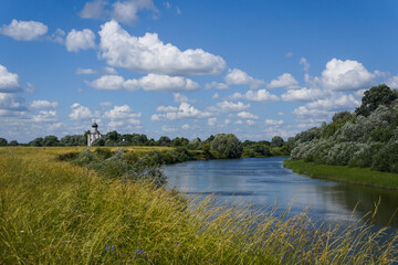 Fototapeta na wymiar Countryside landscape with church, meadow, river and sky with white clouds in summer