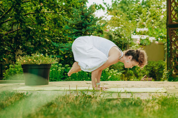 Woman practices yoga in summer garden: Kakasana, Crow Pose, with bent arms