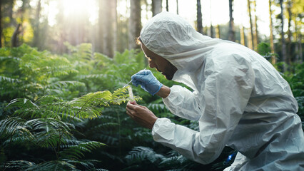 Biologist with white protective suit takes samples on new plants in the forest - obrazy, fototapety, plakaty
