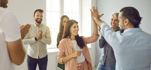 Teamwork concept. Header background with team of cheerful people having fun workshop with business coach. Happy positive man and woman giving each other high five standing in office among coworkers