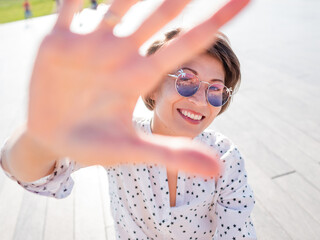 Wind ruffles short hair of freckled woman in colorful sunglasses. Smiling woman at open wooden...