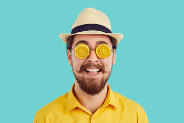 Studio headshot of happy young man in funny bizarre fruit shaped sunglasses. Head shot of bearded mustached hipster guy wearing yellow shirt, summer hat and eccentric glasses designed as orange slices