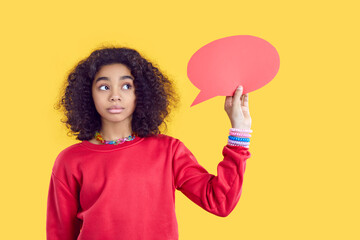 Paper blank speech bubble in hands of pensive african american teen girl on yellow background. Cute...