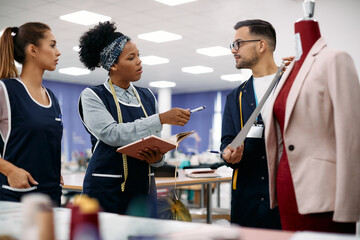 Group of clothing designers cooperate while making plans for new line in textile factory.