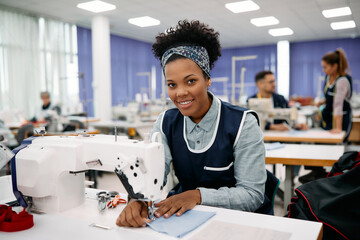 Happy black dressmaker sewing while working on production line in a factory.