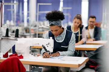 Young black woman works as seamstress at production line in textile factory.